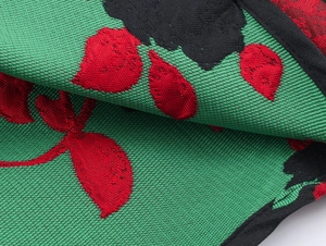 Gros plan sur le tissu en maille jacquard vert aux motifs floraux rouges et noirs