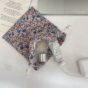 Detail view of floral drawstring pouch showing hand cream and perfume bottle storage