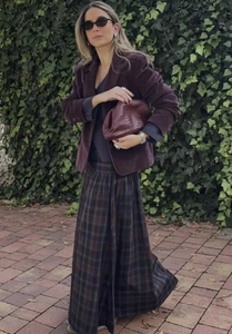 Dettaglio di blazer in velluto a coste viola scuro con gonna a quadri e borsa in pelle intrecciata