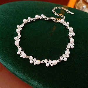 Macro view of irregular zircon and pearl bracelet on a dark green velvet display