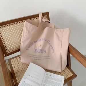 Large pink canvas tote bag with floral and letter embroidery shown on a wooden chair