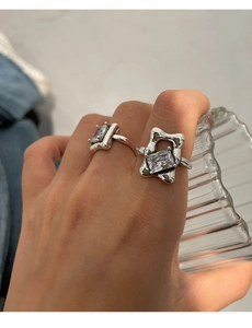 Detail of silver geometric rings with square zircons on female hand holding glass