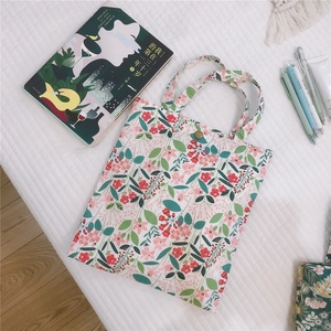 Vue à plat d'un mini sac cabas en toile à fleurs roses sur un tissu blanc matelassé