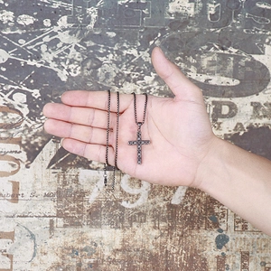 Gros plan d'un pendentif croix en acier inoxydable vintage tenu dans la main