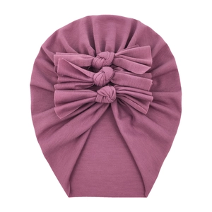 Detail of purple cotton baby hat featuring three decorative bows and soft knit texture