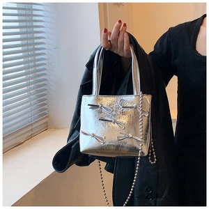 Detail of silver pleated handbag featuring chic ribbon bows and a detachable metal chain strap