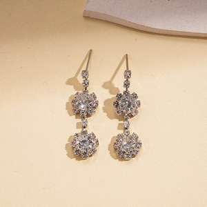 Detailed view of silver flower-shaped rhinestone drop earrings on textured background