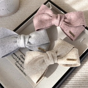 Close-up of three velvet bow hair clips in pink, grey and beige with gold handmade tags