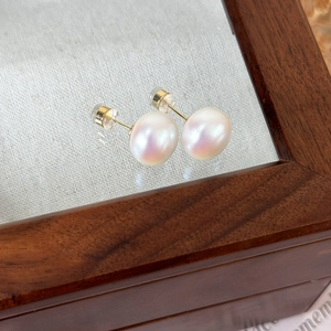 Detailed close-up of pink pearl stud earrings with golden pins on a wood and fabric base