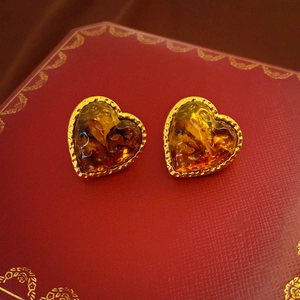 Macro shot of amber resin heart earrings with beaded gold edges on a red luxury gift box
