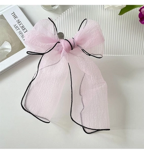 Detail of pink pleated organza scarf with black edges styled as a bow on a white desk
