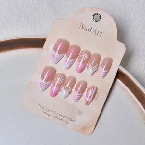 Detail of 3D almond press-on nails with snowflakes, pink diagonal stripes and bows