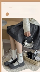 Detail of white cotton mid-calf socks featuring ruffle edges and delicate bow accents