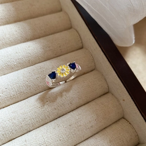 Detailed shot of open ring featuring blue heart gems and yellow enamel flower in jewelry box