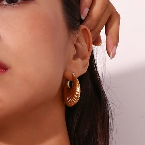Macro detail of gold hollow earrings showing twisted texture and polished metal sheen