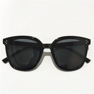 Detail of oversized black sunglasses featuring three signature metallic dots on the frame