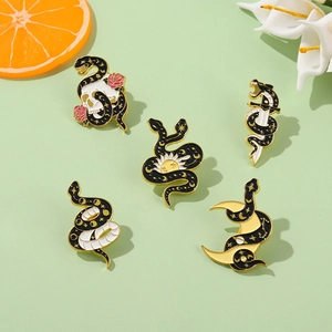 Detail of five dark gothic snake enamel pins with skull, rose and sun motifs on a green background