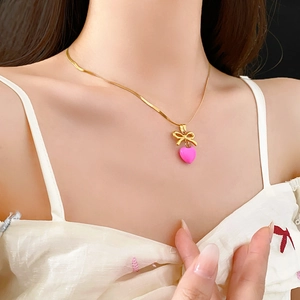 Collier chaîne serpent dorée avec pendentif cœur rose et nœud sur un mannequin