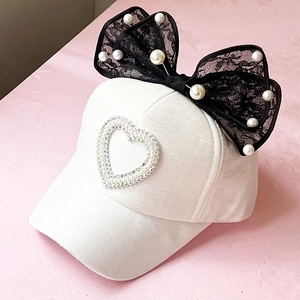 Detail of white girl's sun hat featuring black lace bow and heart-shaped pearl accents