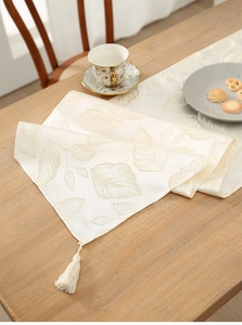 Detail of beige leaf jacquard table runner with fringe on a wooden dining table