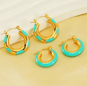 Detail of gold-plated hoop earrings featuring green enamel inlay on silk background