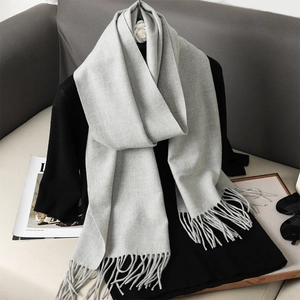 Detail view of a soft grey cashmere-feel scarf with elegant fringe trim on a display stand
