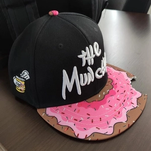 Detail of black snapback hat with THE MUNCHIES embroidery and pink donut bite notch brim