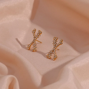 Detail of gold X-shaped stud earrings featuring sparkling pave-set zircons on silk fabric