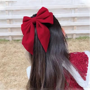 Large red fabric bow hair clip shown on girl's long dark hair with outdoor background