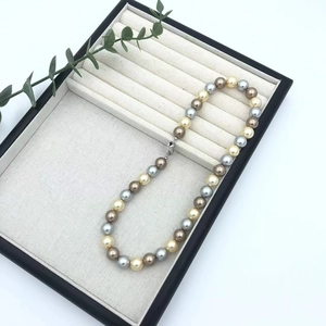 Macro shot of multi-colored pearls in beige jewelry tray with elegant green plant accent