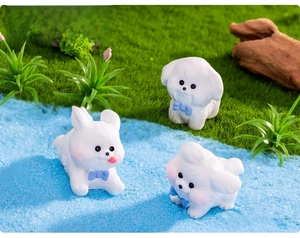 Three cute miniature white resin puppies with blue bows on artificial grass landscape