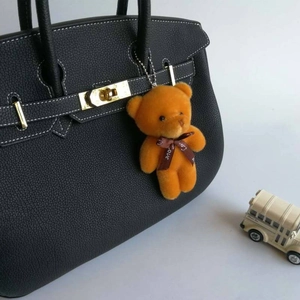 Orange teddy bear plush keychain with Love ribbon hanging on a black handbag