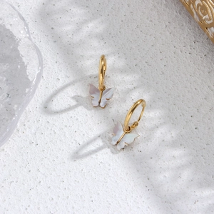 Detail of golden hoop earring featuring a white shell butterfly pendant on sand texture