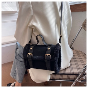 Close-up of black plush cylinder handbag with leather straps and gold buckle detail