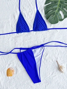 Flat lay of blue mesh bikini with side-tie bottoms on sand with tropical leaves