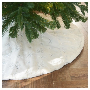Close-up of white plush Christmas tree skirt with silver sequin snowflakes on wood floor