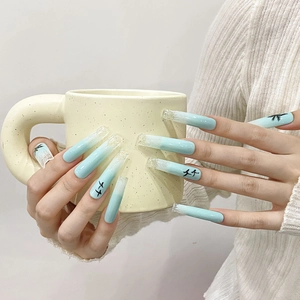 Extra long blue gradient press-on nails with palm tree art shown on a coffee cup