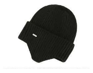 Detail of black ribbed knit winter beanie with earflaps and silver metal logo plaque