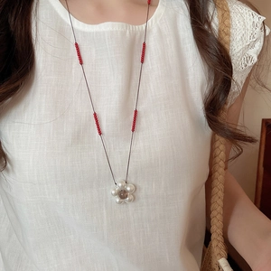 Macro detail of handmade floral necklace featuring white pearl petals and red beaded cord