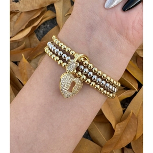 Dettaglio di braccialetti impilati con perle d'oro e d'argento e un ciondolo a cuore