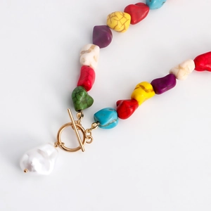 Detailed close-up of colorful irregular stones necklace with baroque pearl and gold toggle clasp