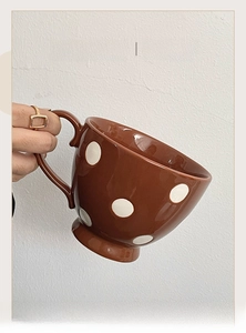 Détail montrant une main tenant un mug vintage en céramique à pois blancs et glaçure brune