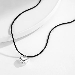 Minimalist s925 silver heart pendant on a black cord necklace over a white background