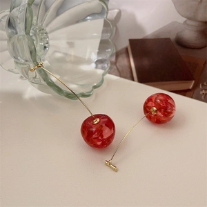 Close-up of red cherry earrings with gold stems placed on a vintage book