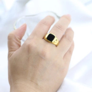 Detailed view of a wide gold stainless steel ring with a square black stone inlay on hand