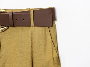 Dettaglio dei pantaloni in raso senape con cintura marrone e bottone in metallo dorato
