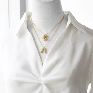 Detail of layered gold necklaces with zircon-encrusted A and C letter pendants