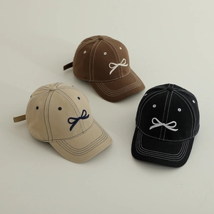 Détail de la broderie de nœuds sur des casquettes en coton marron, beige et noir