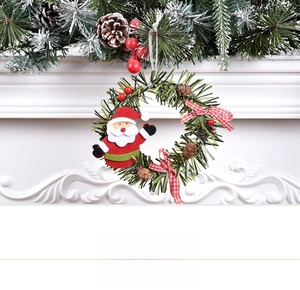 Close-up of Christmas wreath with Santa doll, pine cones and red berries on white fireplace
