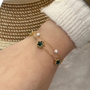 Gold layering bracelet with emerald stars and pearls on a female model wrist